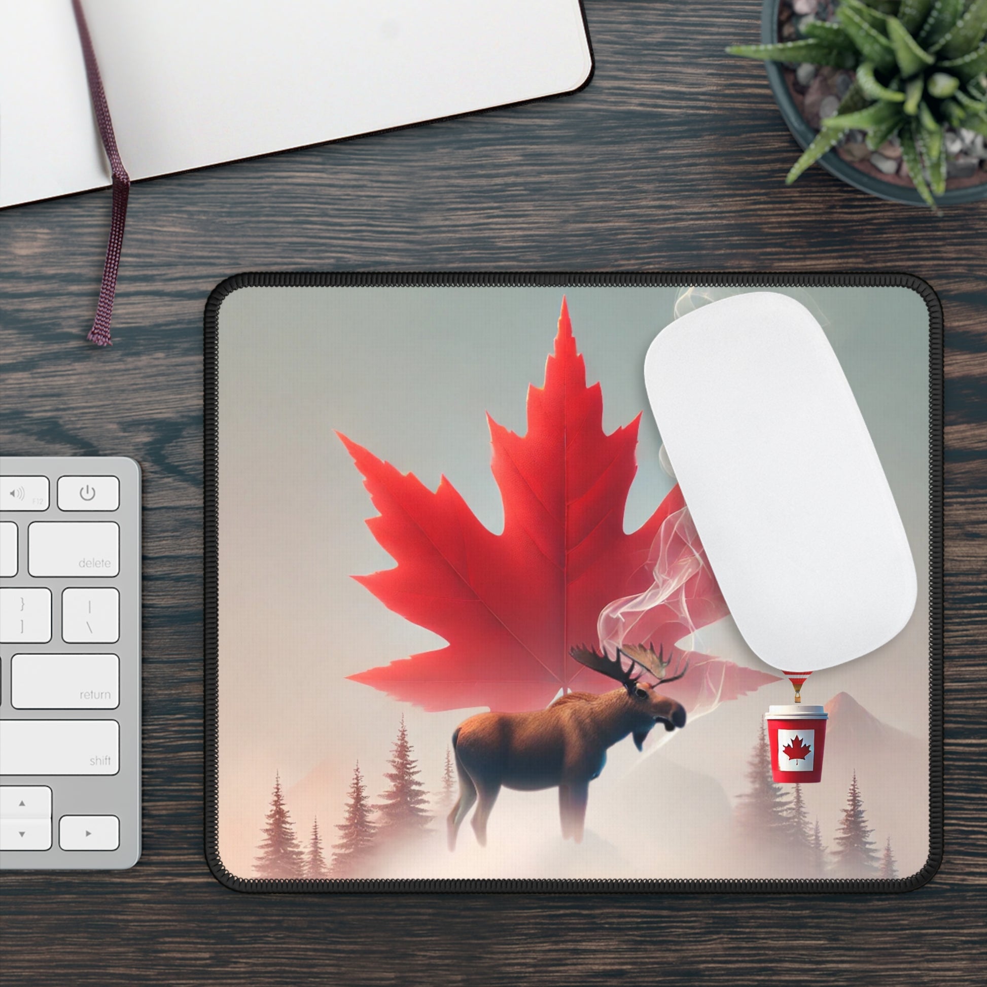 Mouse pad with a red maple leaf and moose design on a desk with a keyboard and plant.