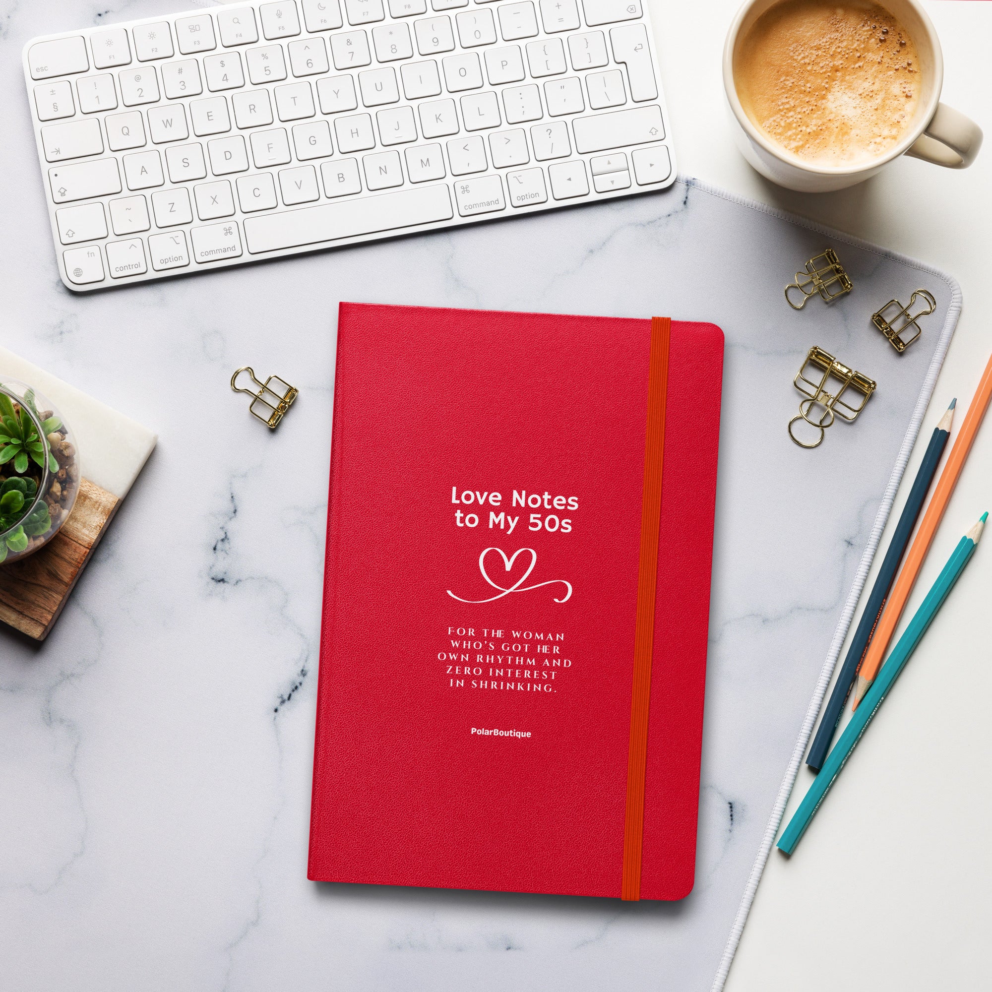 Red notebook titled 'Love Notes to My 50s' on a marble desk with office supplies.