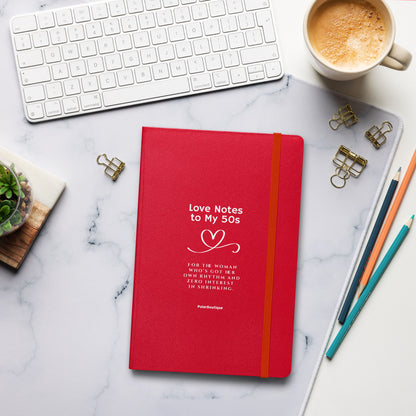 Red notebook titled 'Love Notes to My 50s' on a marble desk with office supplies.