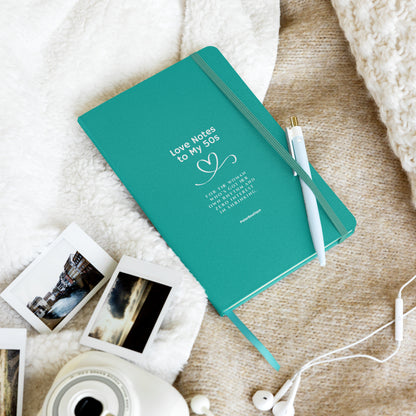 Teal notebook with 'Love Notes to My 50s' text on a textured surface with photos and a camera.
